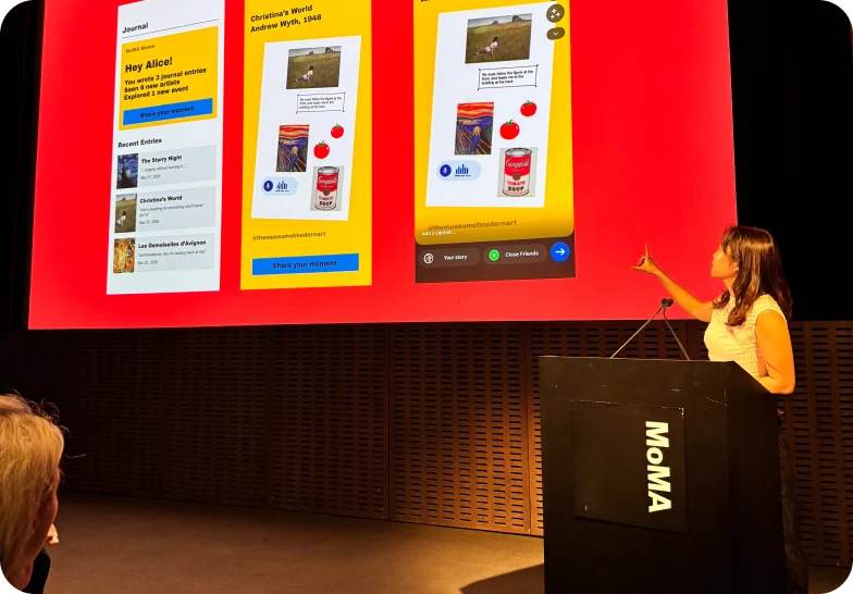 A speaker at a MoMA lectern presenting three large wayfinding screens projected on a red backdrop.