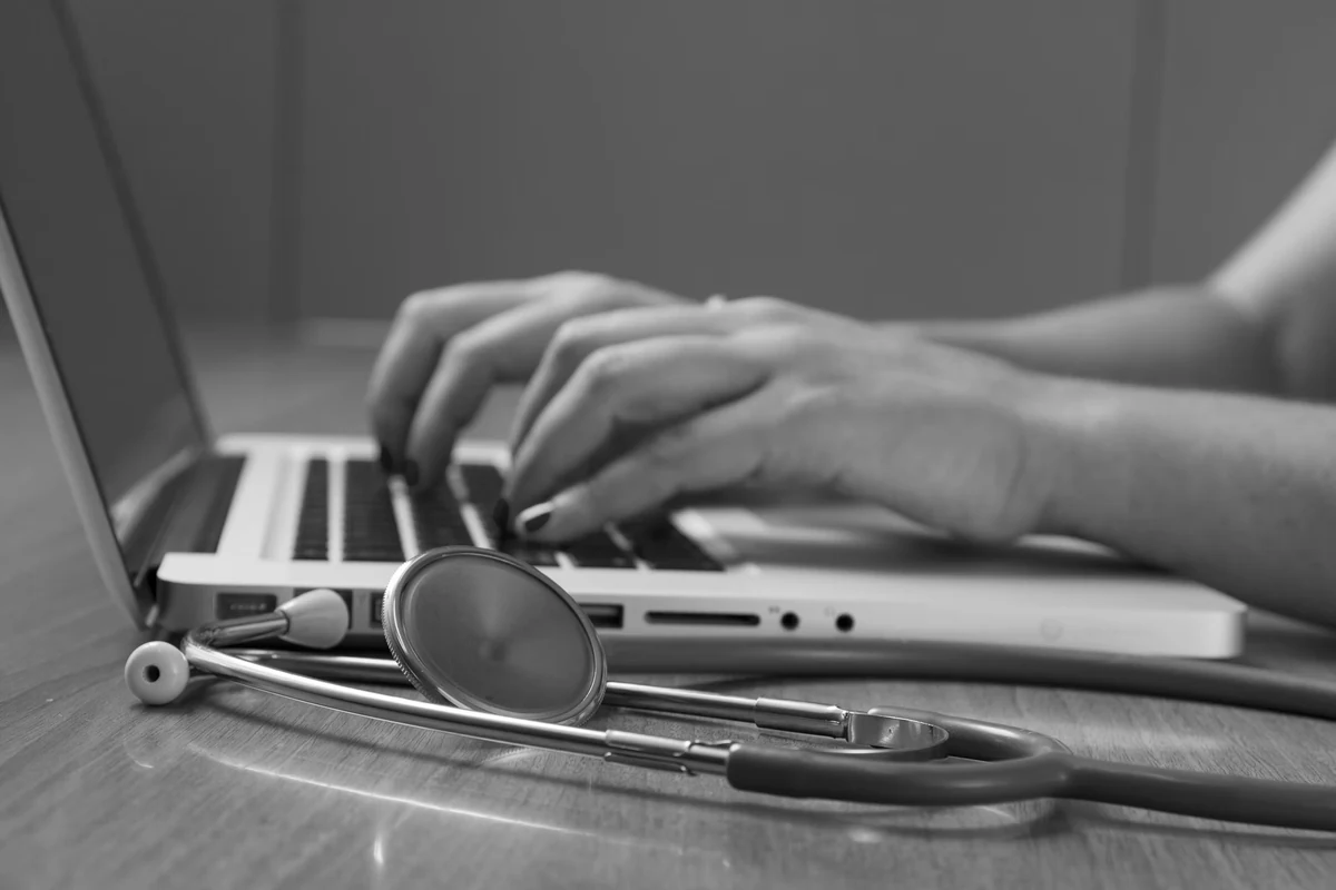 A clinician typing on a laptop beside a stethoscope