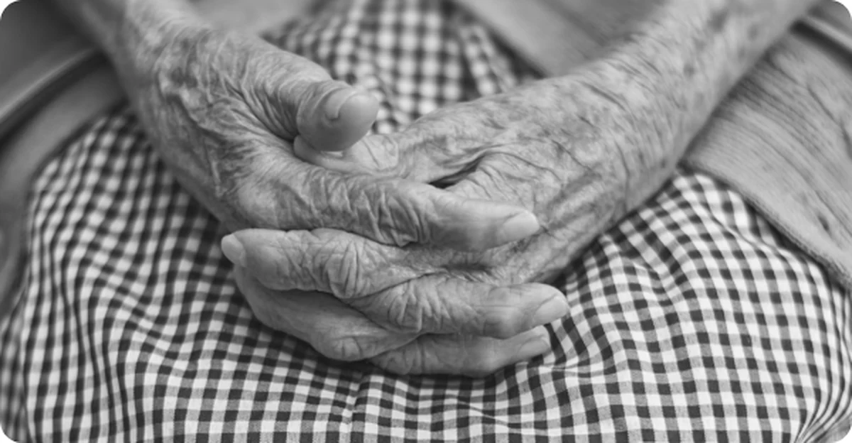An older patient's clasped hands resting in their lap