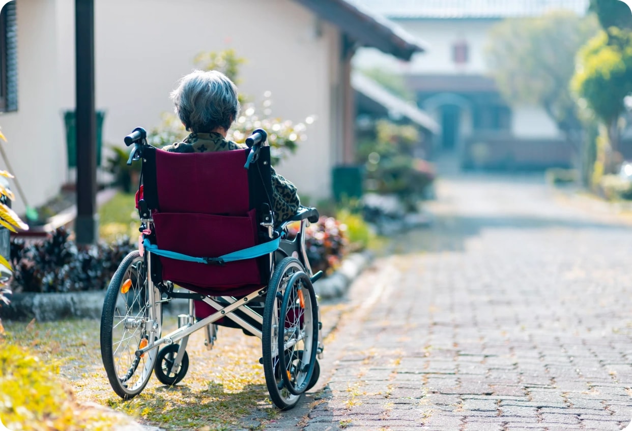A patient in a wheelchair outdoors on a garden path